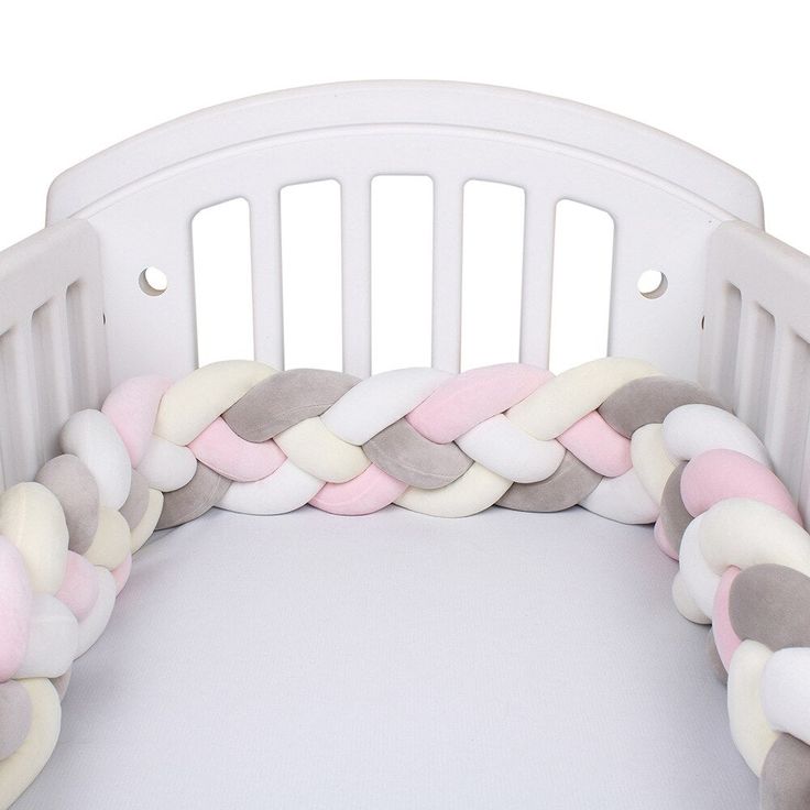 a white crib with pink, grey and white pillows on it's sides