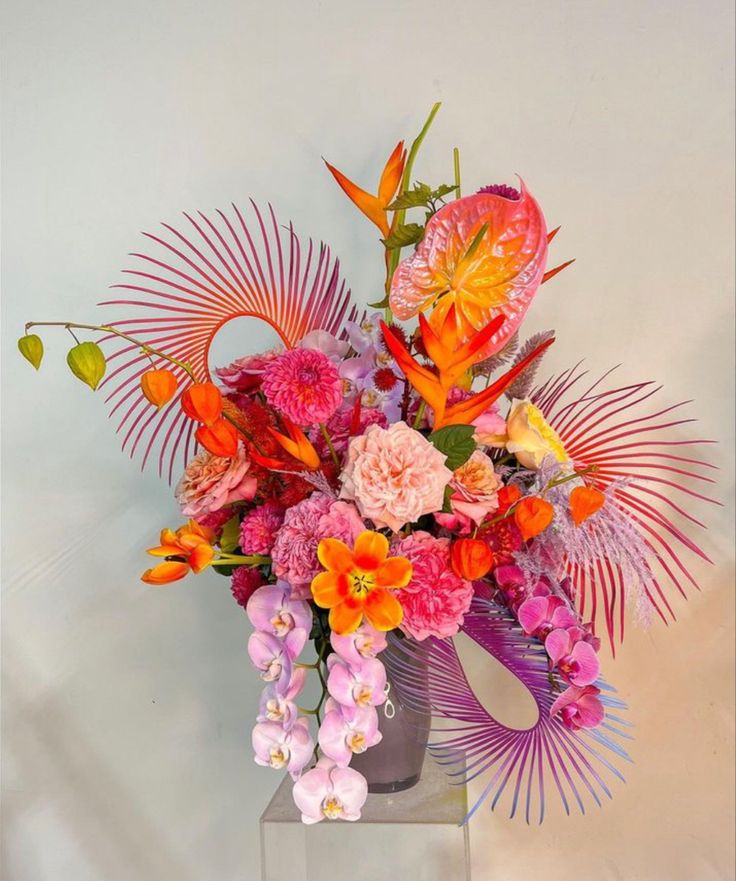 a vase filled with lots of colorful flowers on top of a white table next to a wall