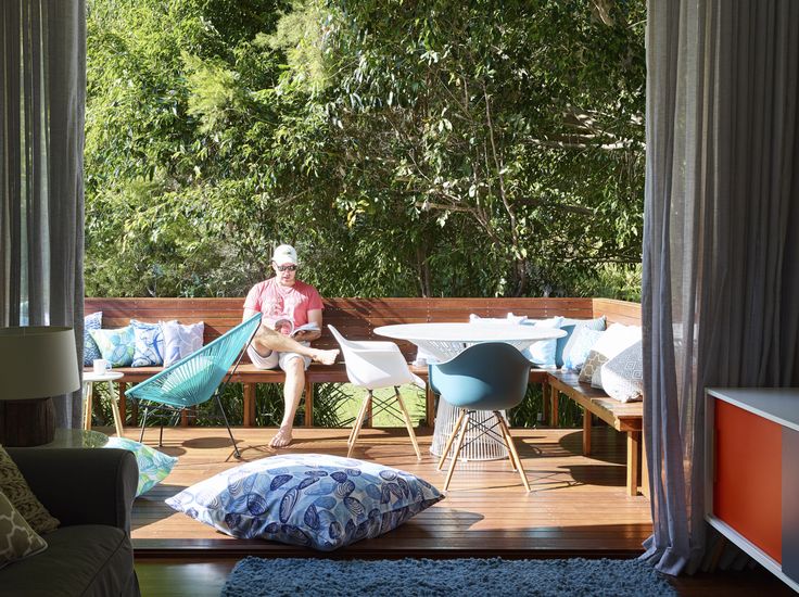 a man sitting on a wooden deck next to a table and chairs with blue cushions