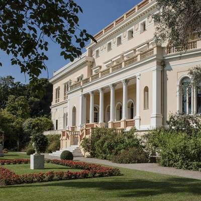 a large white house with many windows and balconies on the front lawn, surrounded by greenery