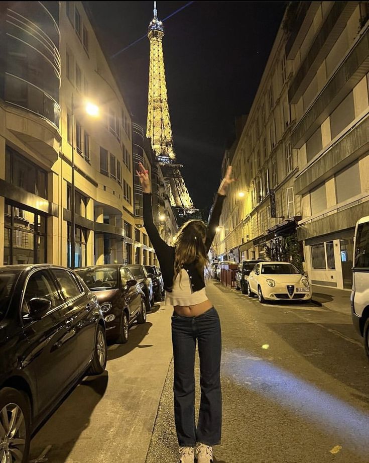 a woman standing on the side of a street in front of a tall eiffel tower