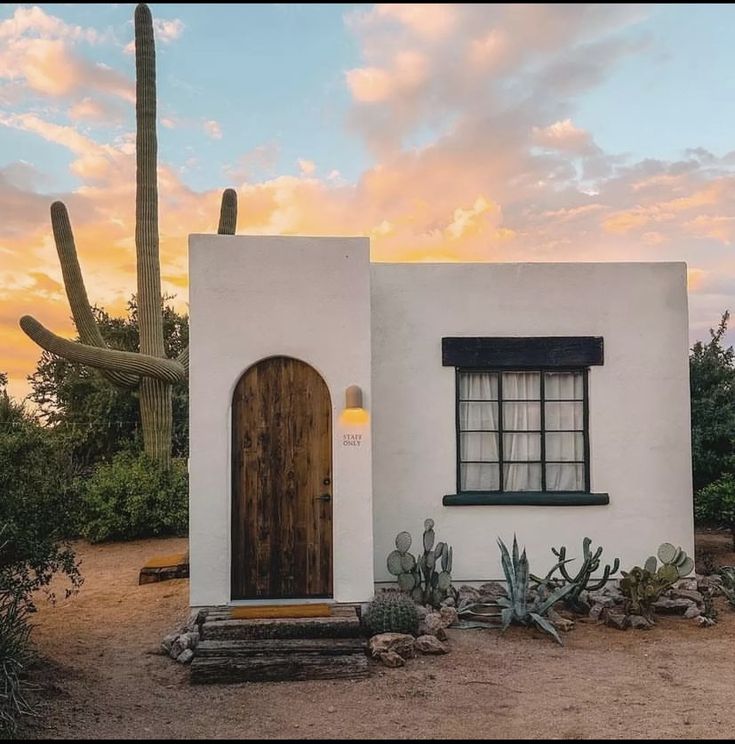 a white adobe house with cactus and cacti in the foreground at sunset