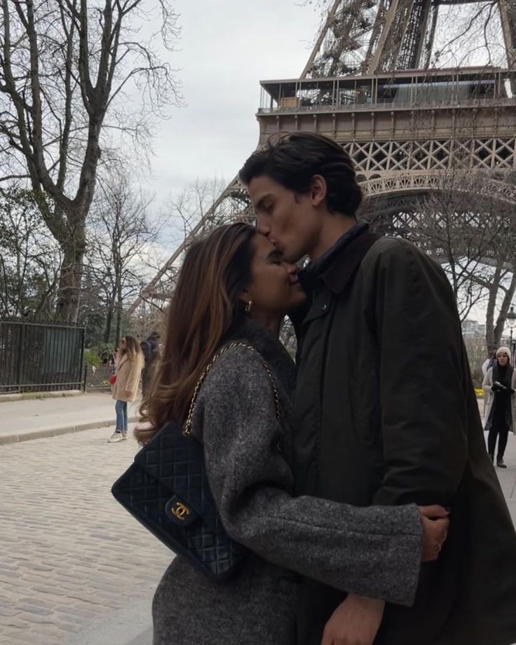 a man and woman standing in front of the eiffel tower kissing each other