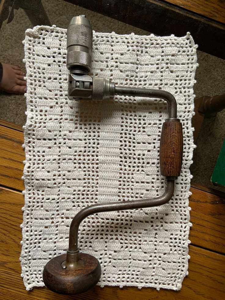 an old fashioned sewing machine on top of a white knitted placemat with a wooden handle