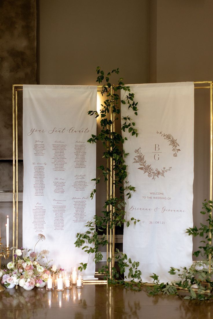 a table with candles, flowers and greenery next to two large white linens