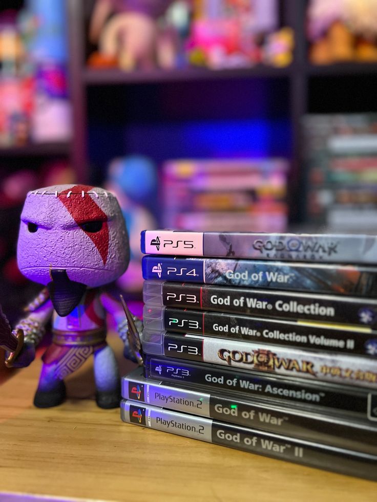 a stack of video game dvds sitting on top of a wooden table next to a stuffed animal