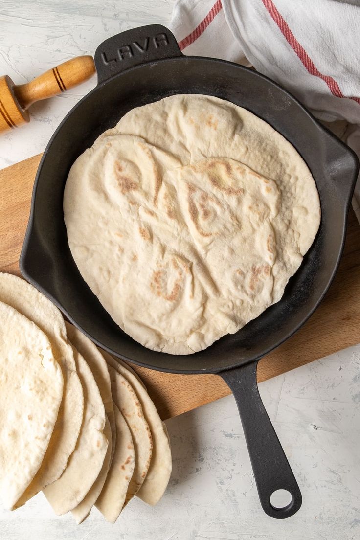 a skillet filled with tortillas sitting on top of a wooden cutting board