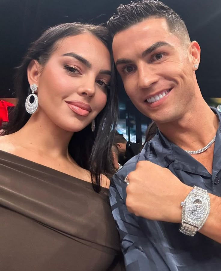 a man standing next to a woman in a brown dress and diamond watch on her wrist