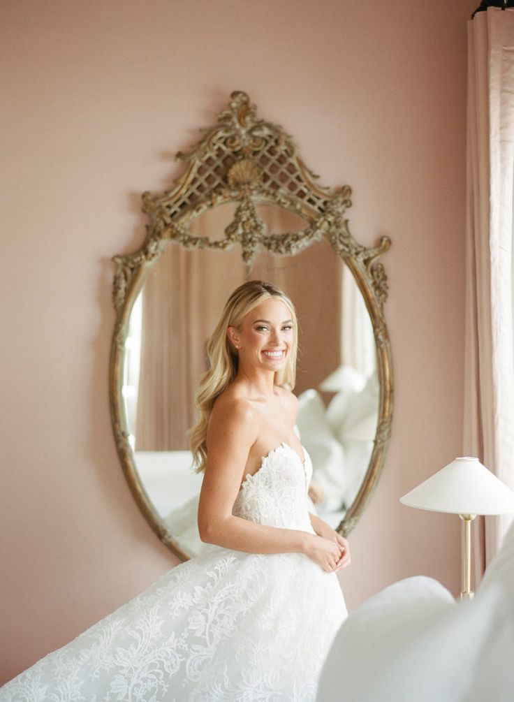 a woman in a white wedding dress standing in front of a mirror and looking into the camera