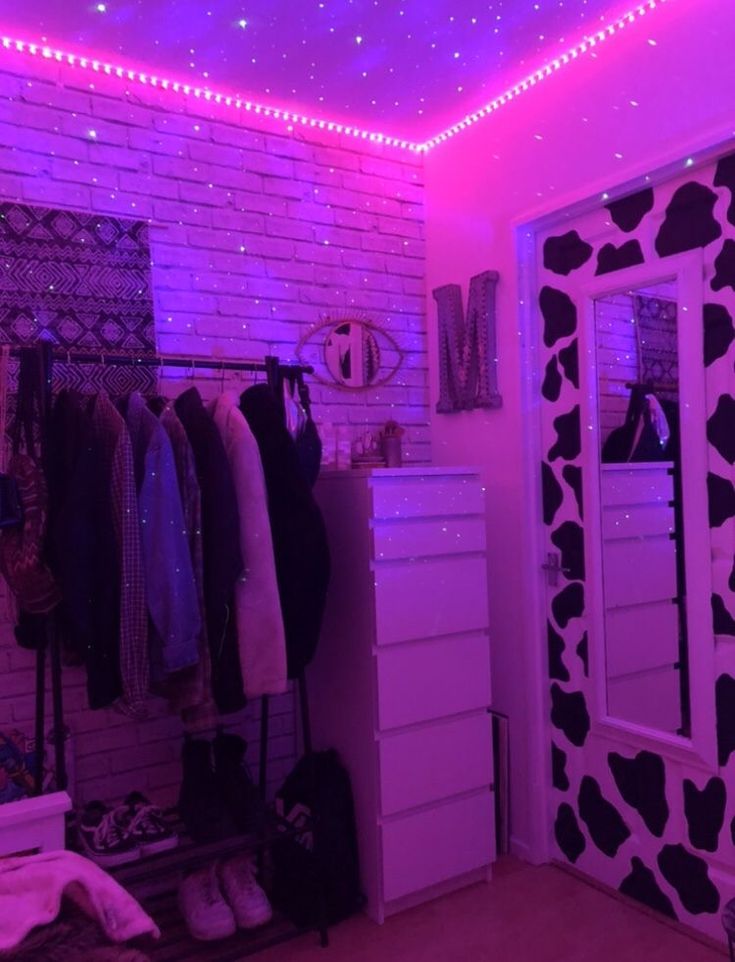 a room with purple lights and clothes hanging on the rack, in front of a white brick wall