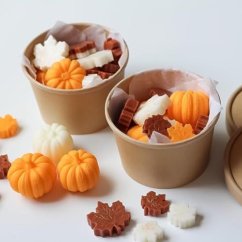 two cups filled with candy and candies on top of a white table next to small pumpkins