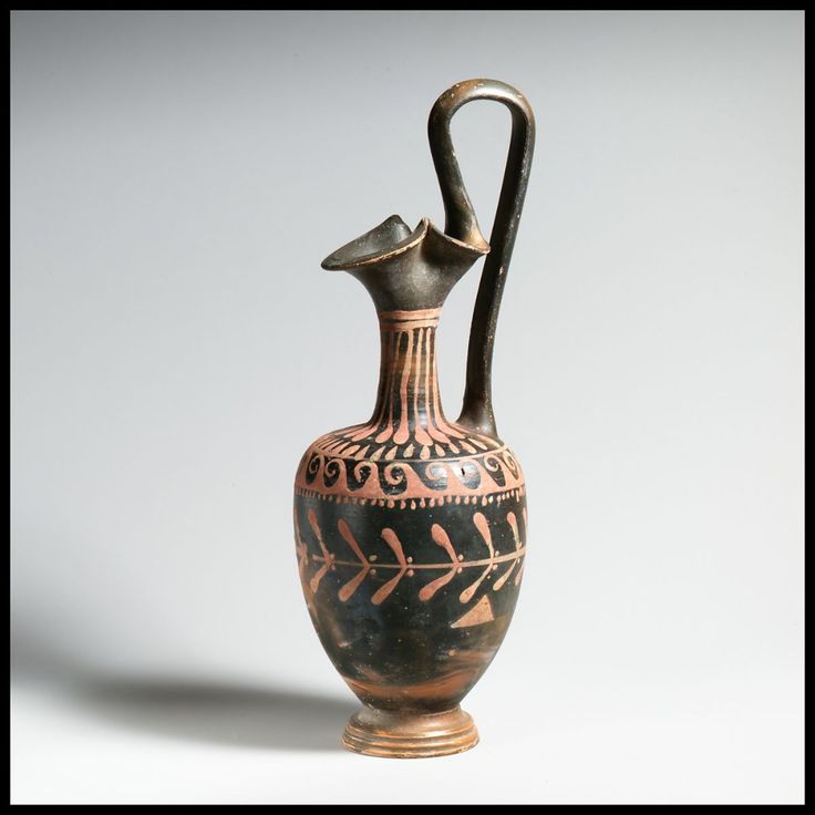 an old black and gold vase with a bird on it's handle, sitting on a white surface