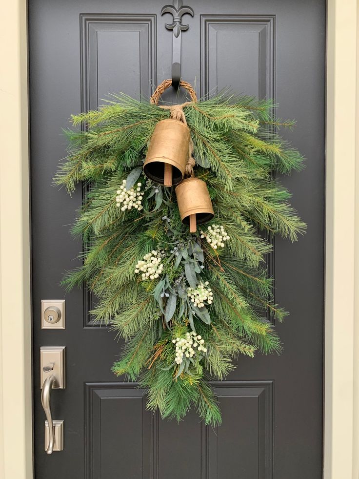 a christmas wreath with bells hanging on the front door and evergreen leaves, berries, and white flowers