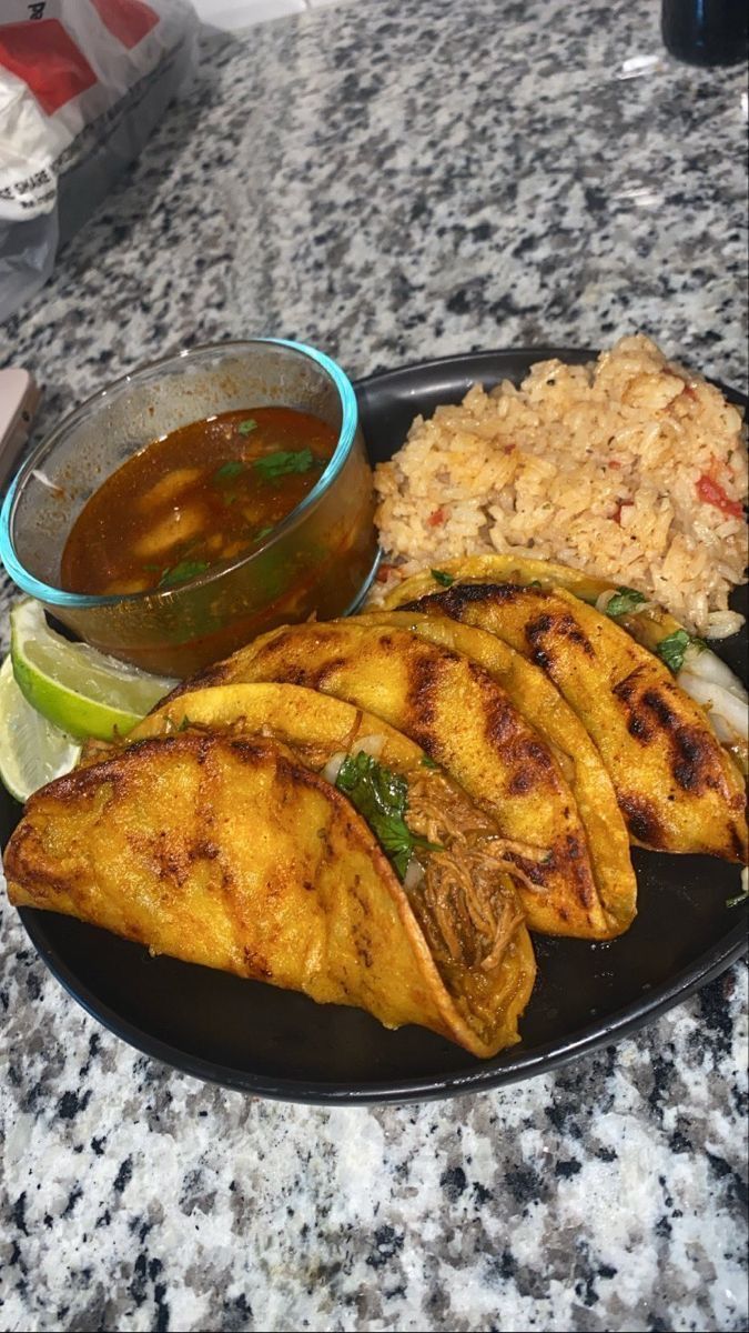 some food is sitting on a black plate and next to a bowl of dipping sauce