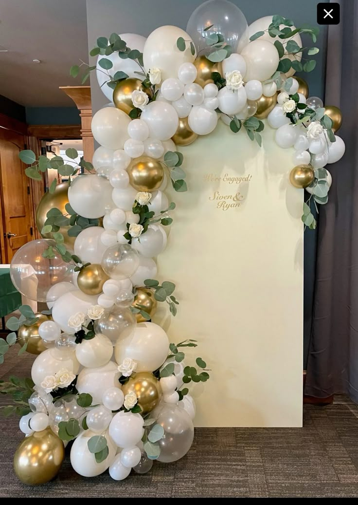 the balloon arch is decorated with white and gold balloons, greenery, and flowers