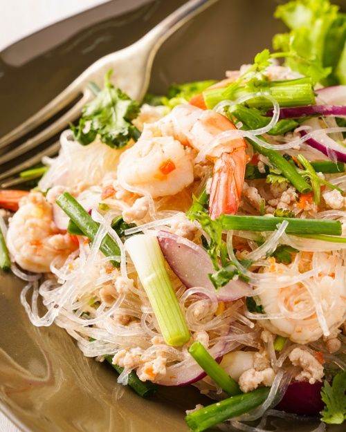 a salad with shrimp, lettuce and carrots on a plate next to a fork