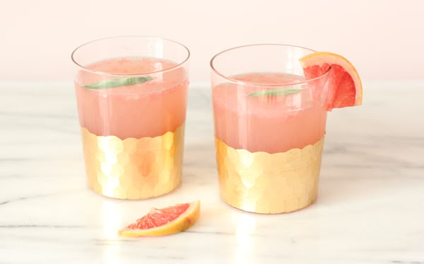 two glasses filled with watermelon and gold rimmed drinks on a marble table