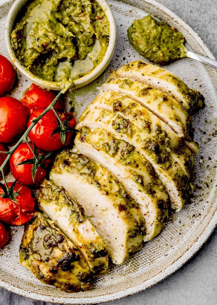 a plate with chicken, tomatoes and pesto sauce