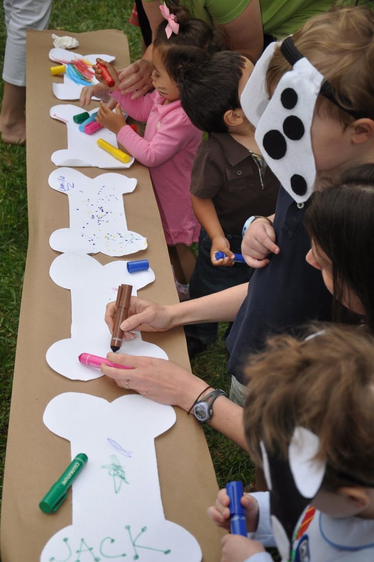 a group of children sitting at a long table with paper cutouts on it and crayons in front of them