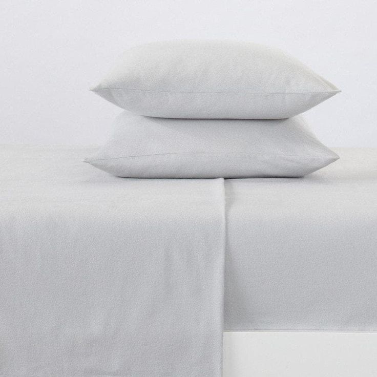 two white pillows on top of a bed with sheets and pillowcases in the background