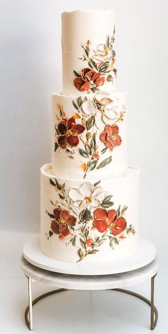 a three tiered white cake with red flowers painted on the top and bottom layer