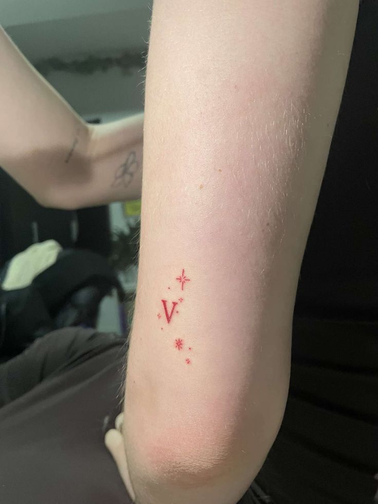 a person with a small tattoo on their arm and the word v is written in red ink