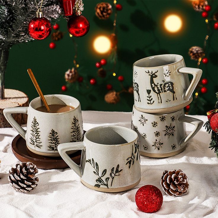 three coffee mugs sitting next to each other on a table with christmas decorations in the background