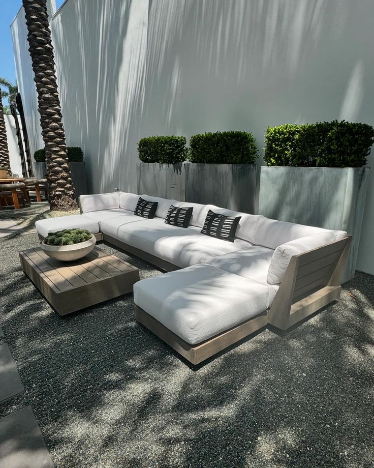 a white couch sitting on top of a stone floor next to a plant filled wall