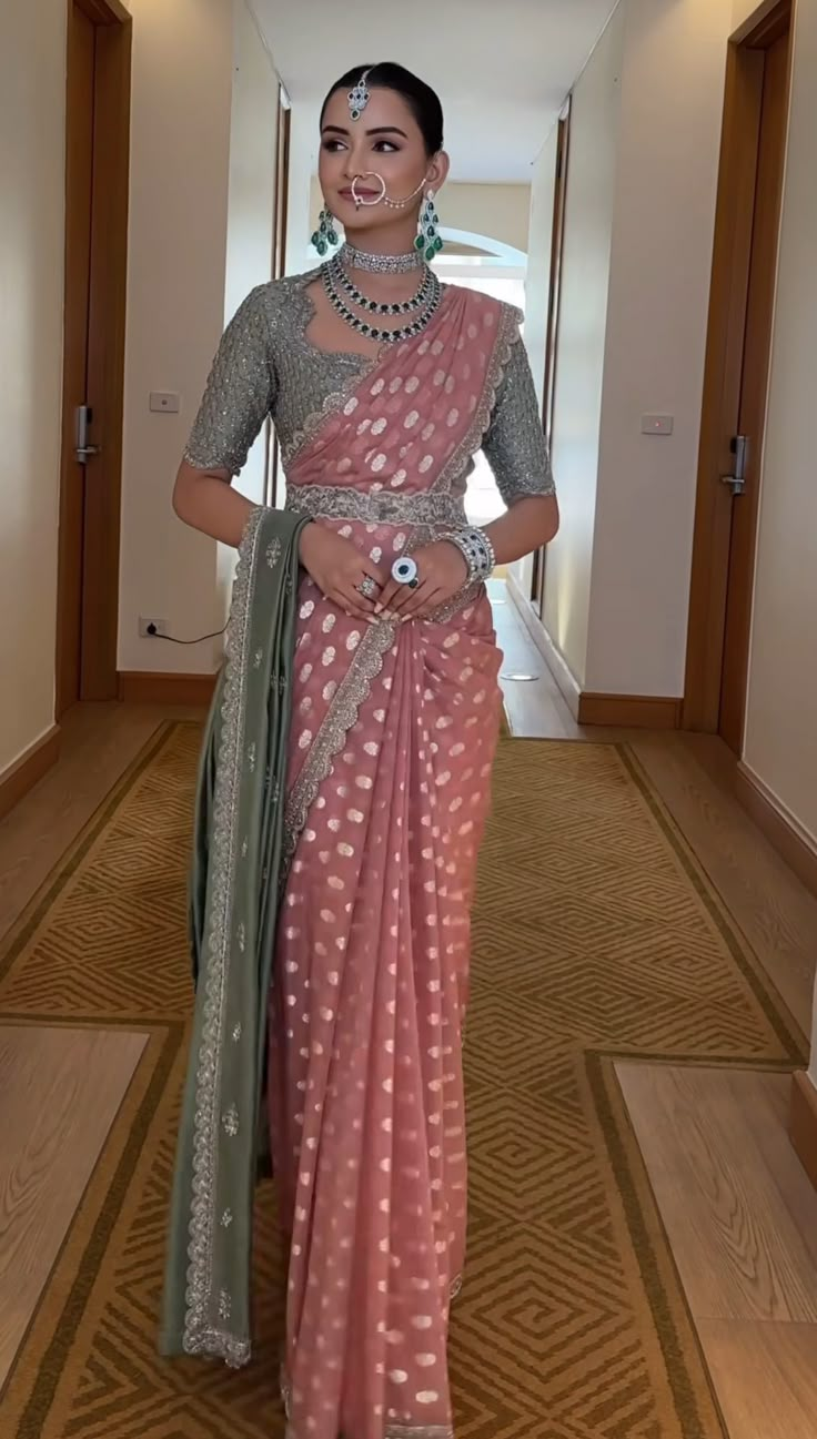 a woman in a pink and green sari is standing on the floor with her hands behind her back