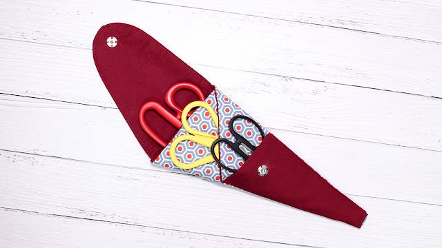 a pair of scissors sitting on top of a piece of red fabric with yellow handles