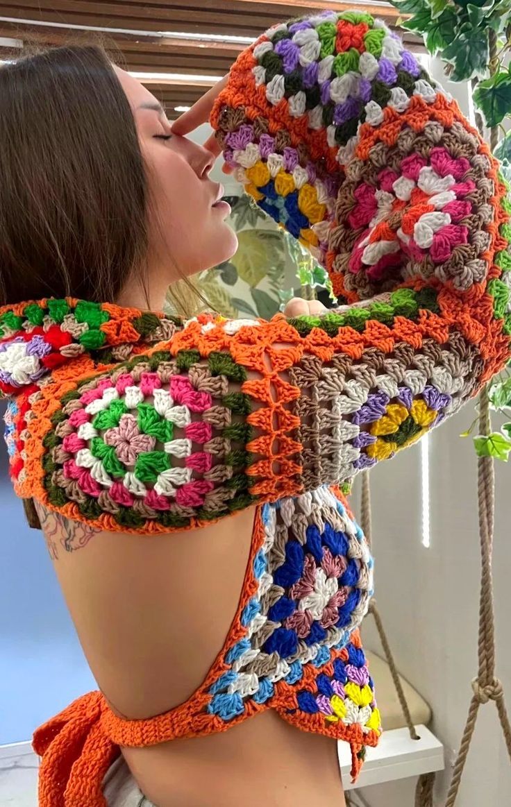 a woman sitting on top of a wooden bench wearing a colorful crochet scarf