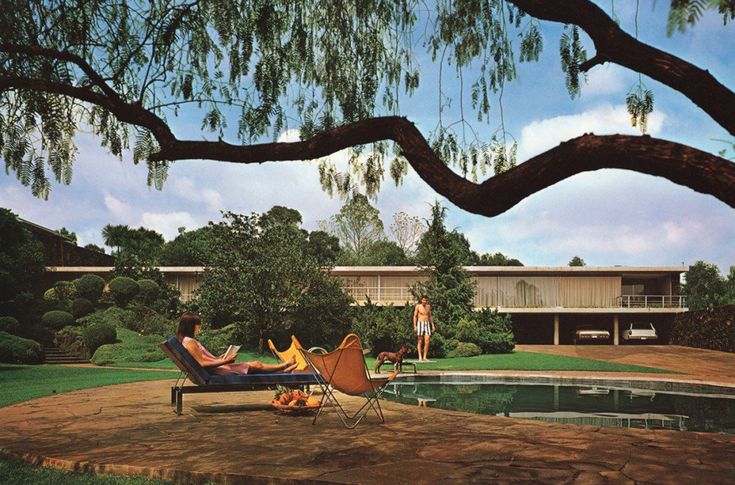 black and white photograph of two people laying on lawn chairs in front of a house