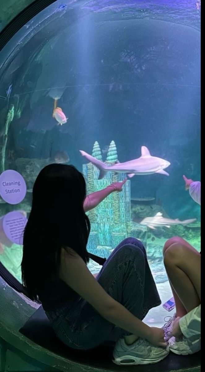 a woman sitting in front of an aquarium looking at fish