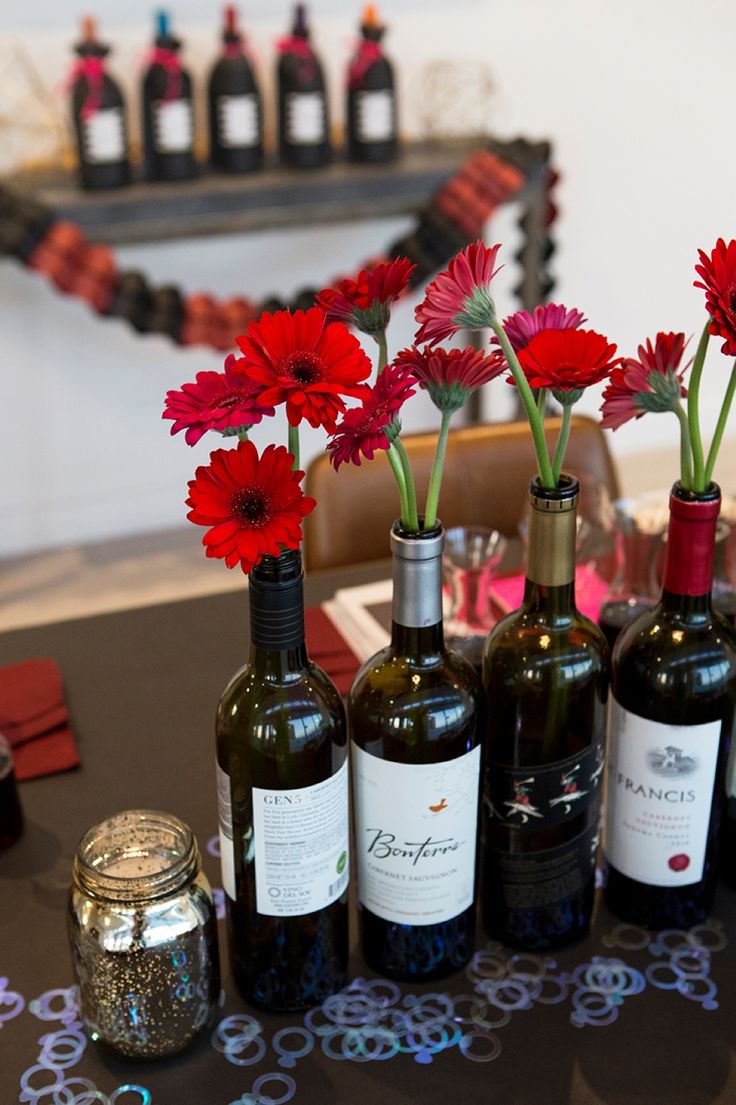 several bottles of wine with red flowers in them on a table next to some jars