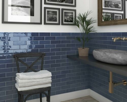 a bathroom with blue tiles and pictures on the wall above the sink, along with a chair