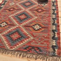 a red and blue rug with fringes on the floor next to a potted plant