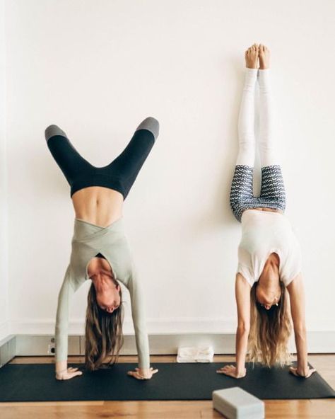 two women doing handstands on yoga mats in front of a white wall and wooden floor