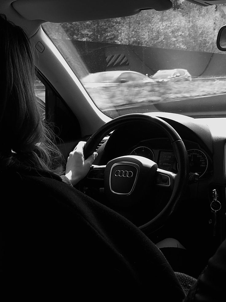 a woman driving a car with her hand on the steering wheel while another person sits in the passenger seat