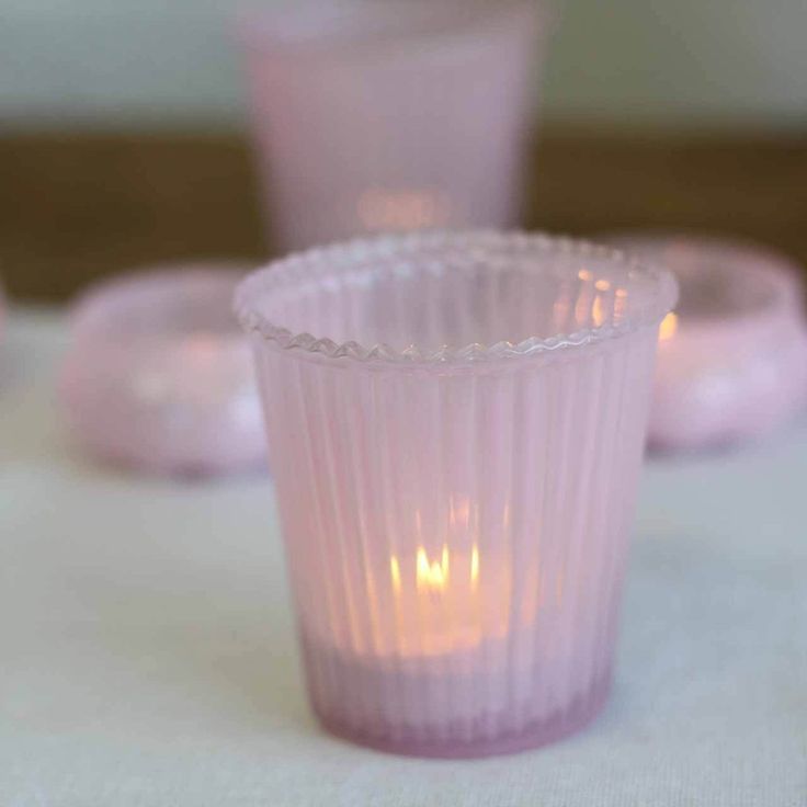 pink glass cups sitting on top of a table next to plates with candles in them