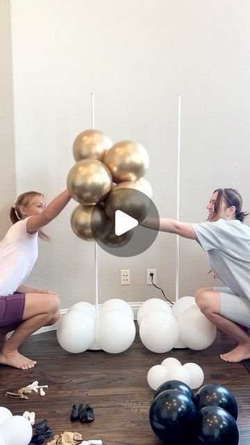 two women are playing with balloons in front of a wall that has white and gold balls on it