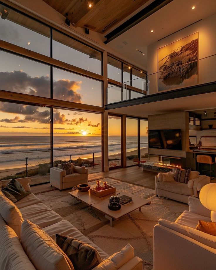 a living room filled with furniture next to a large window overlooking the ocean at sunset