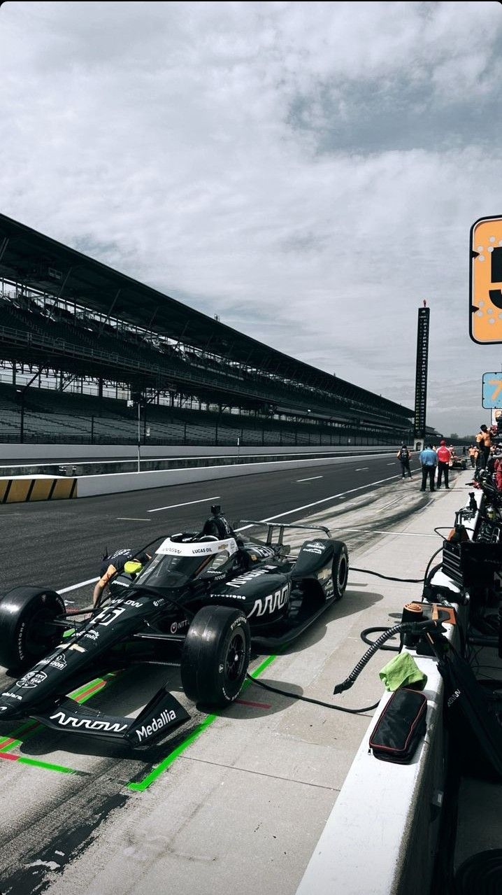 a race car is on the track in front of some people and an orange traffic light