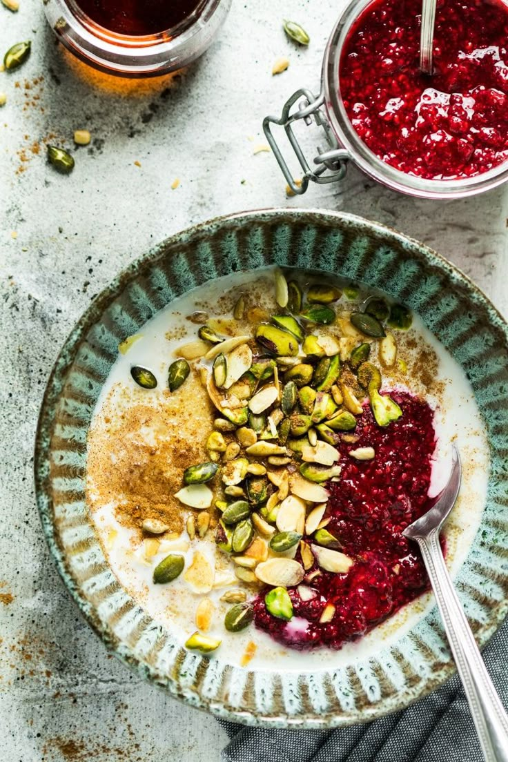 a bowl filled with oatmeal and berries next to two jars of jam