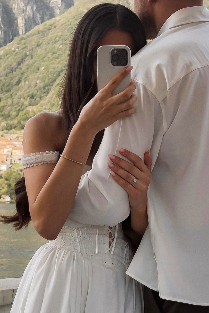 a man and woman standing next to each other in front of a mountain with a cell phone