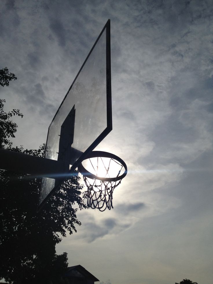 a basketball hoop with the sun shining through clouds in the sky over some trees and houses