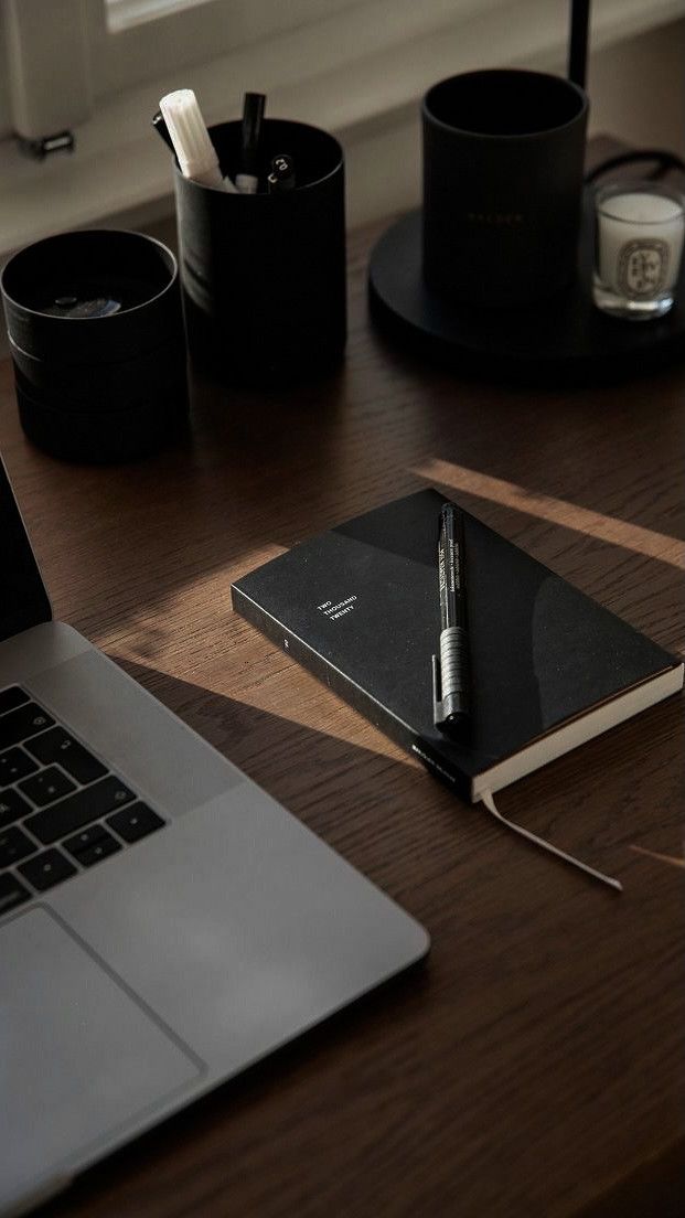 a laptop computer sitting on top of a wooden desk next to a notebook and pen