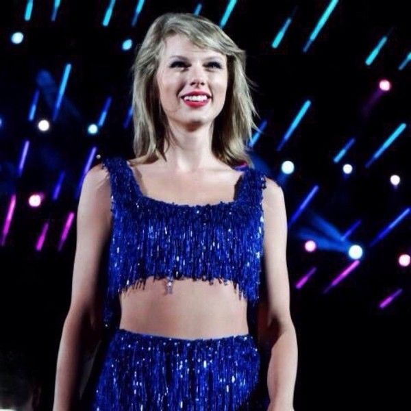 a woman in a blue dress standing on stage with lights behind her and smiling at the camera