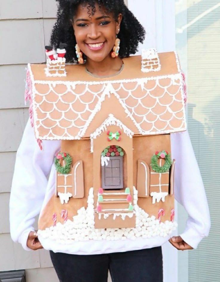 a woman holding up a gingerbread house made to look like it's been built