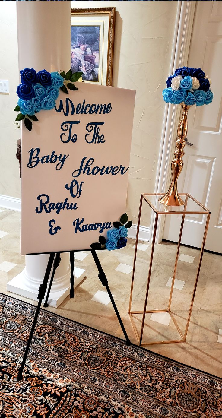 a welcome sign with blue flowers on it in front of a mirror and lamp stand