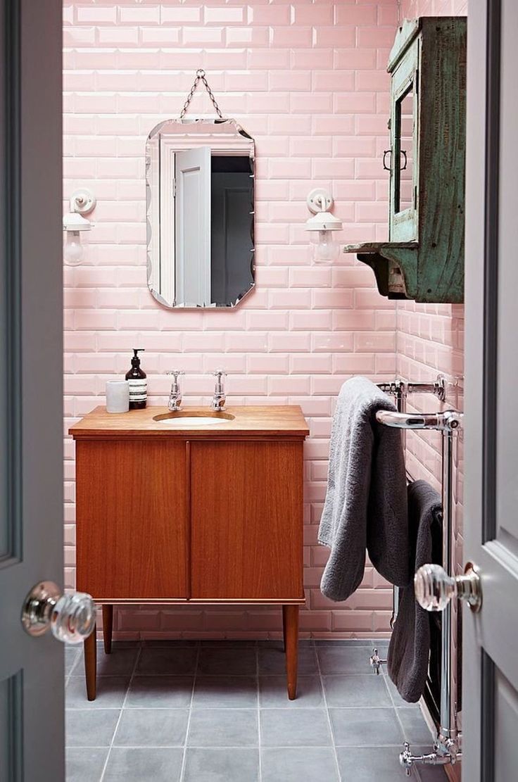 a bathroom with pink brick wall and wooden cabinet, mirror, towel rack and sink